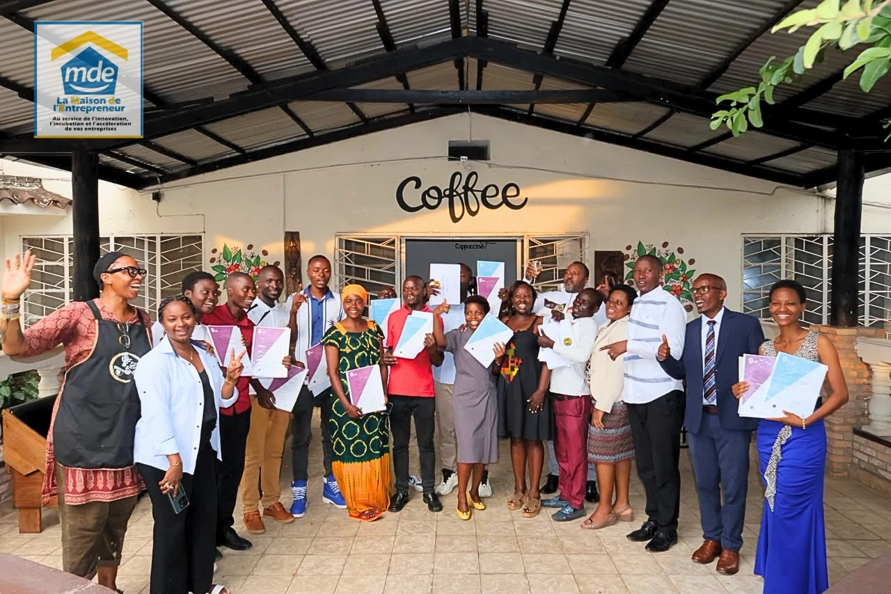 Kawasili barista graduates and ceremony participants celebrating with certificates outside Shamba Kahawa café in Bujumbura