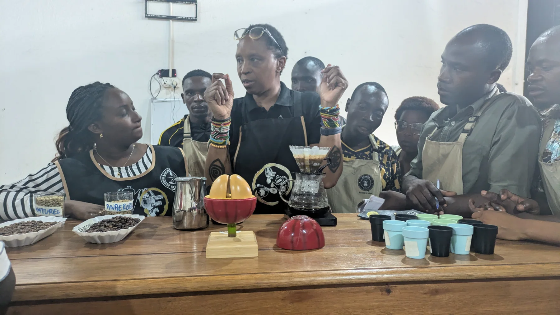 A coffee demonstration with bean samples and tasting cups as Kawasili trainees listen and take notes