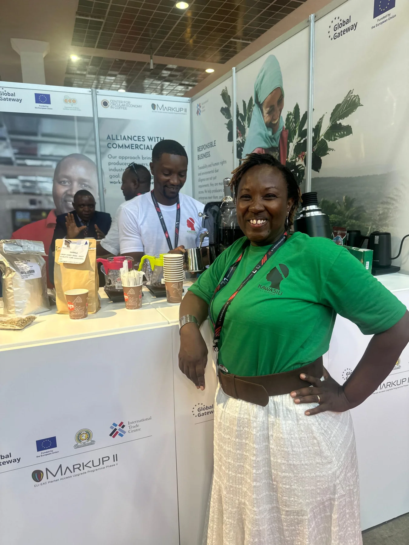 Diane Nsengiyumva wearing a green Kawasili shirt at a coffee stand during World of Coffee Brussels 2026