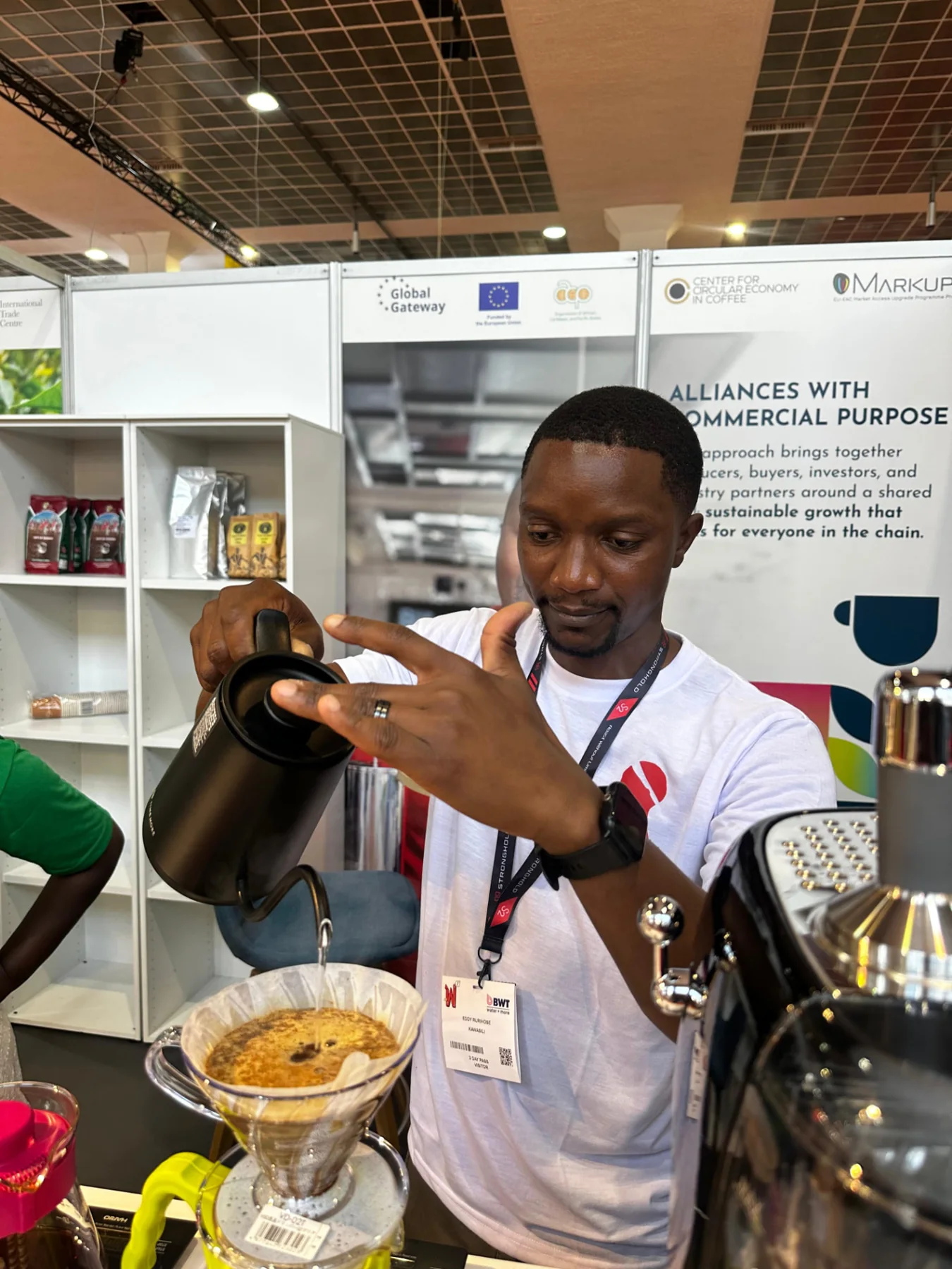 A coffee professional preparing a pour-over at a World of Coffee Brussels exhibition stand