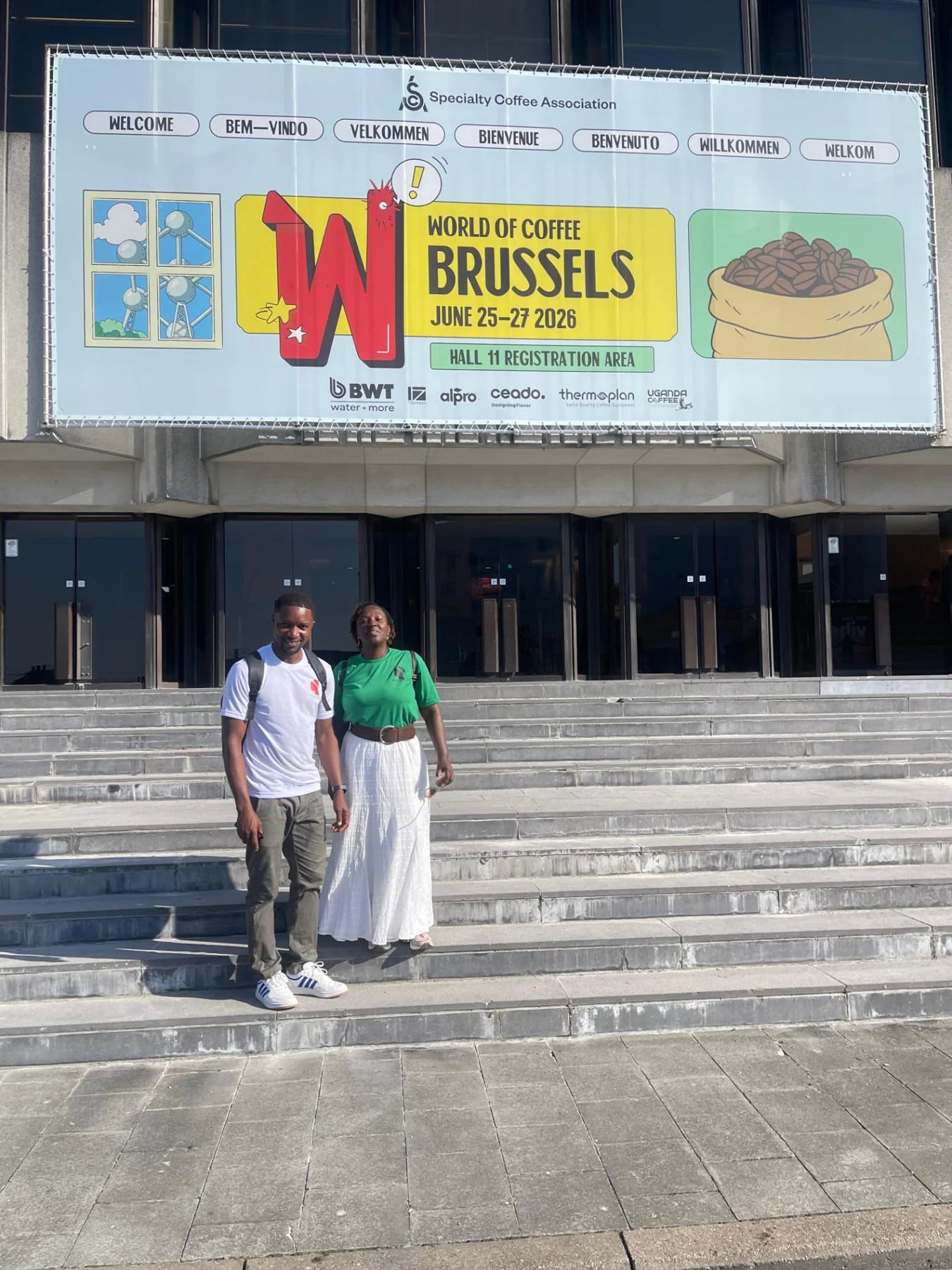 Diane Nsengiyumva and a companion outside Brussels Expo beneath the World of Coffee June 25–27, 2026 banner
